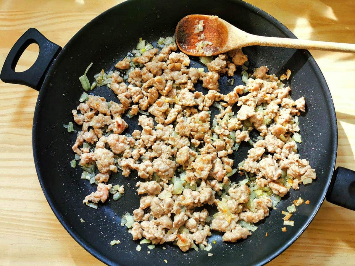 browned sausage and softened onions in a pan