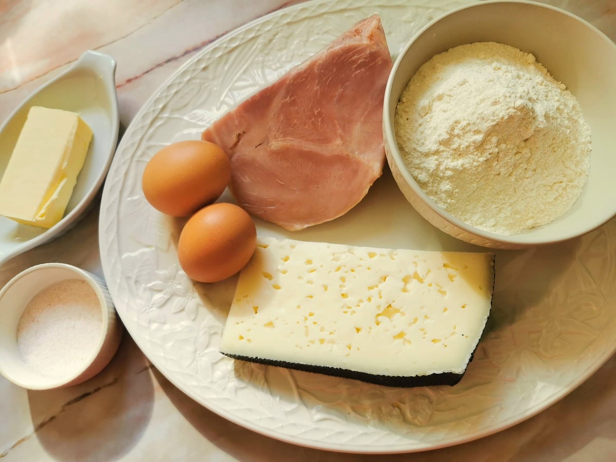 Ingredients for ham and cheese pasta bake with homemade pasta on large white oval plate.