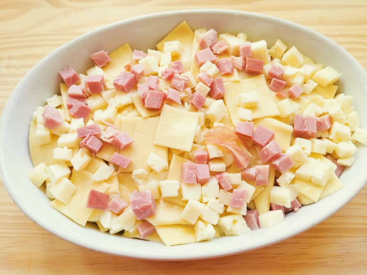 White oval oven dish filled with fresh pasta squares and ham and cheese cubes.