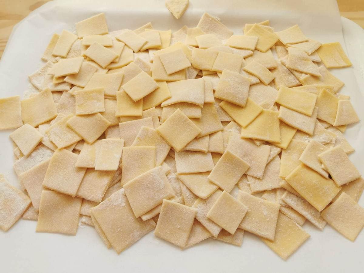 Fresh pasta squares on white baking paper covered tray.