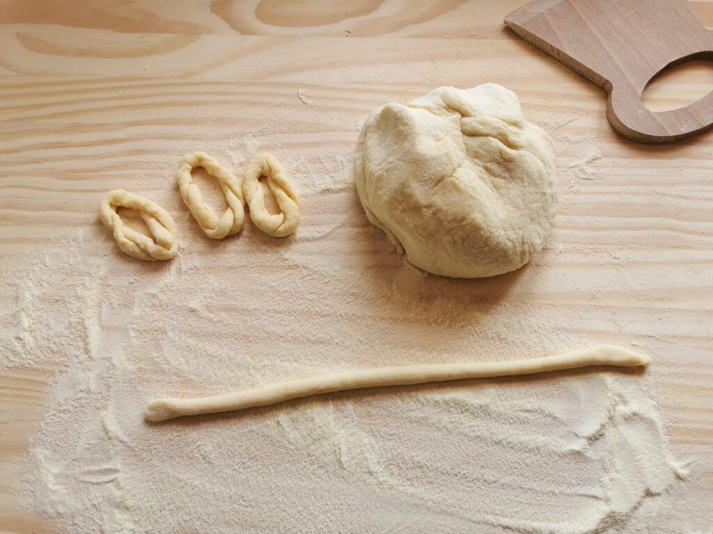 Semolina flour and water dough on wooden pastry board being shaped.