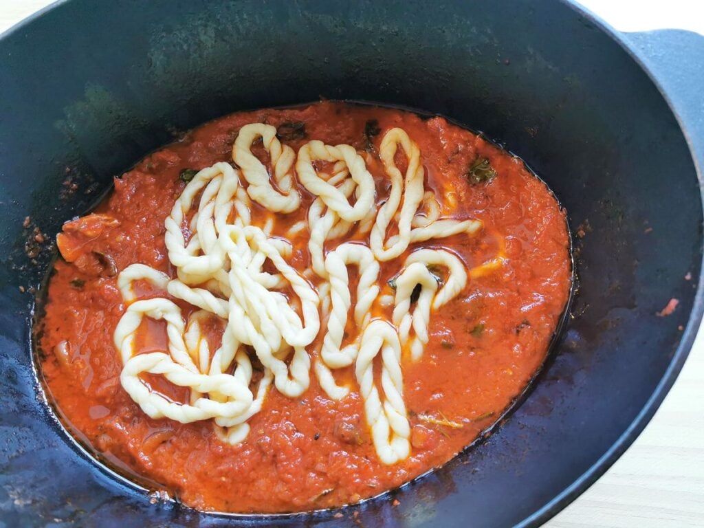 Cooked homemade lorighittas in Dutch oven with sauce after chicken pieces removed.