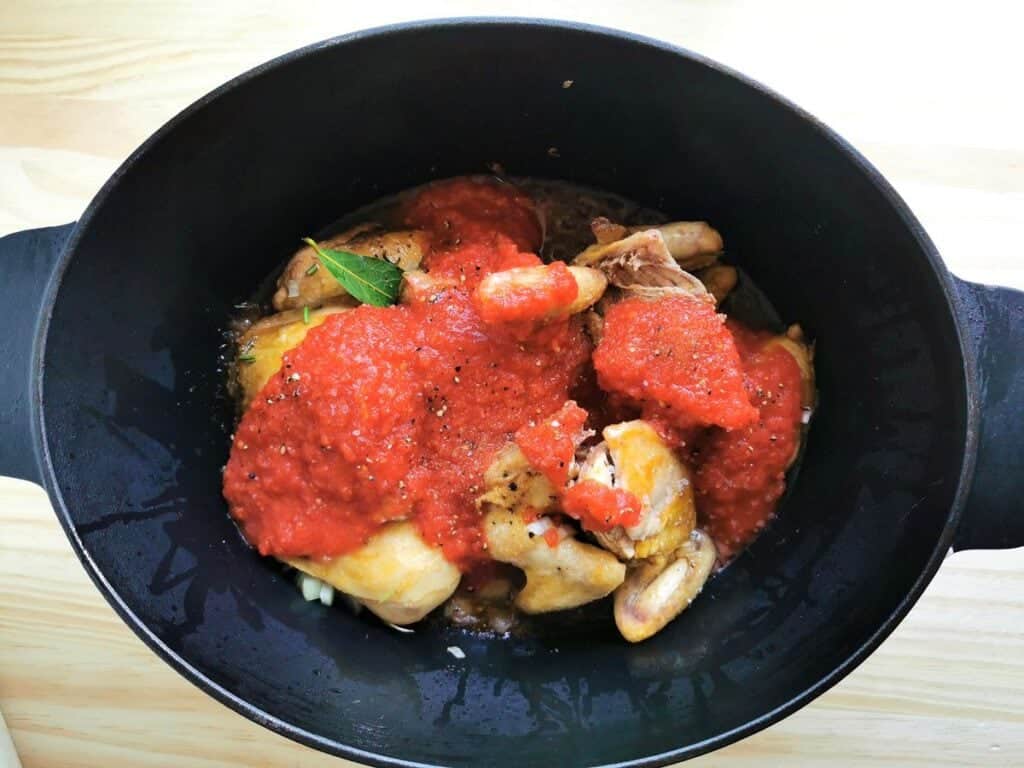 Tomato pulp added to chicken pieces in Dutch oven