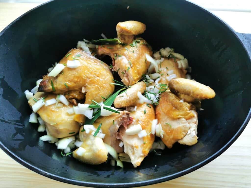 Browned chicken pieces in Dutch oven with chopped onions, garlic and rosemary and bay leaves.