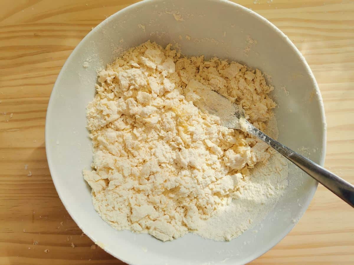 Flour mixed with eggs, water, salt and olive oil mixed together in a white bowl.