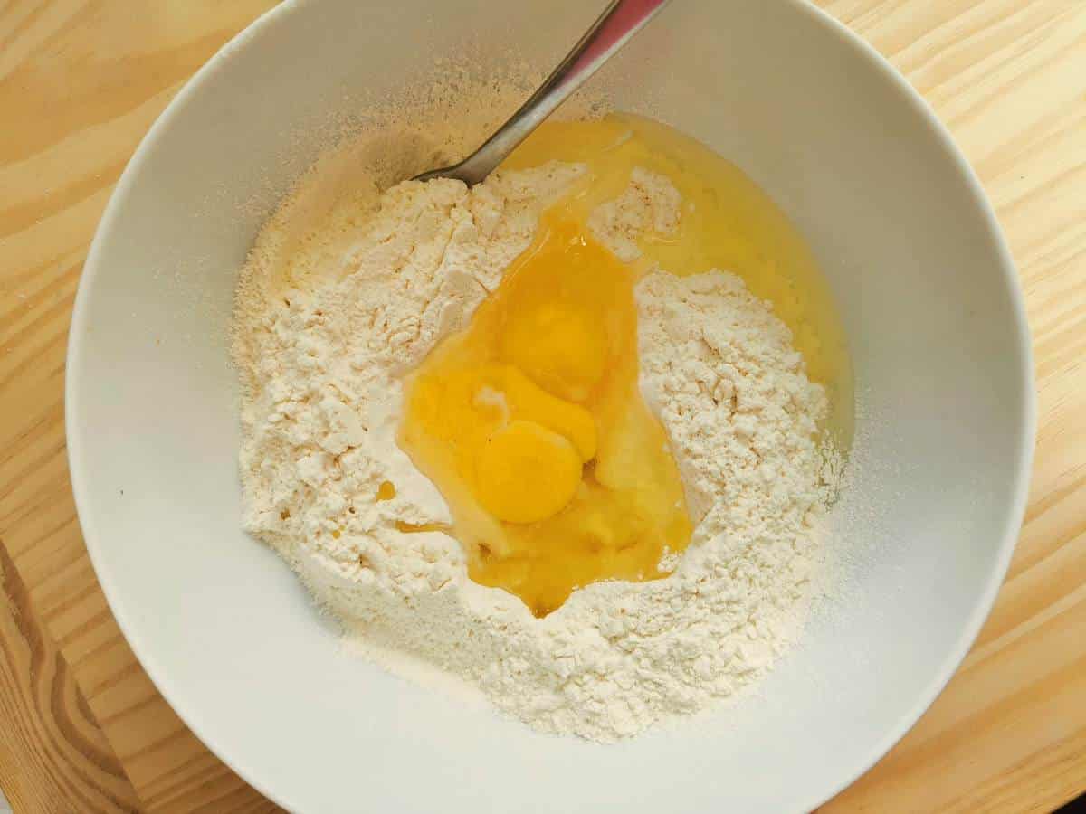 Flour in white bowl with eggs, salt, water and olive oil.