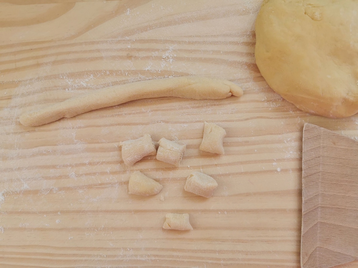 A ball of dough, a long 'rope' of dough and some small 2cm (0.7") pieces of dough on a wood work surface.