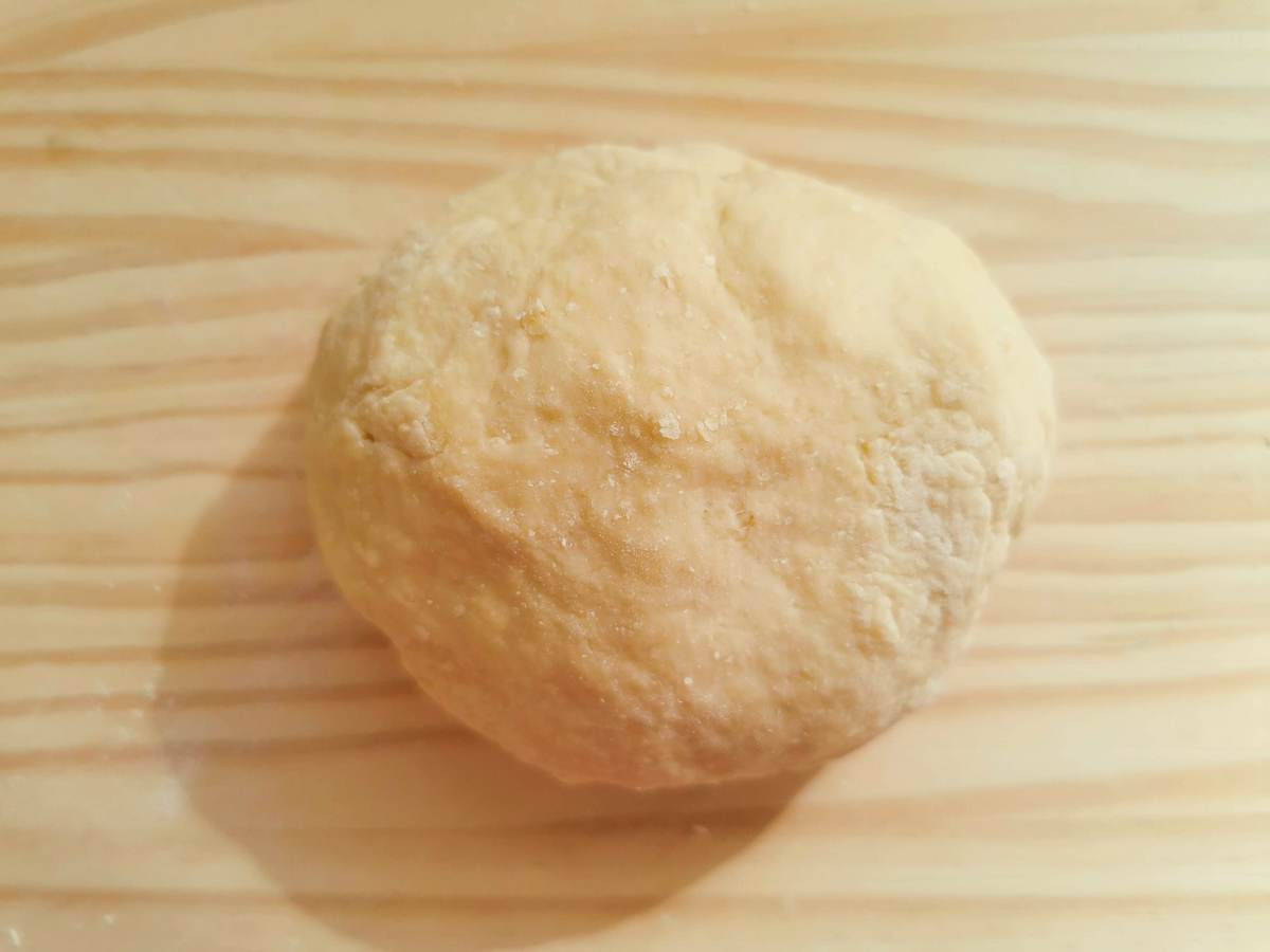 Ball of ready maccheroni dough on wood work surface.