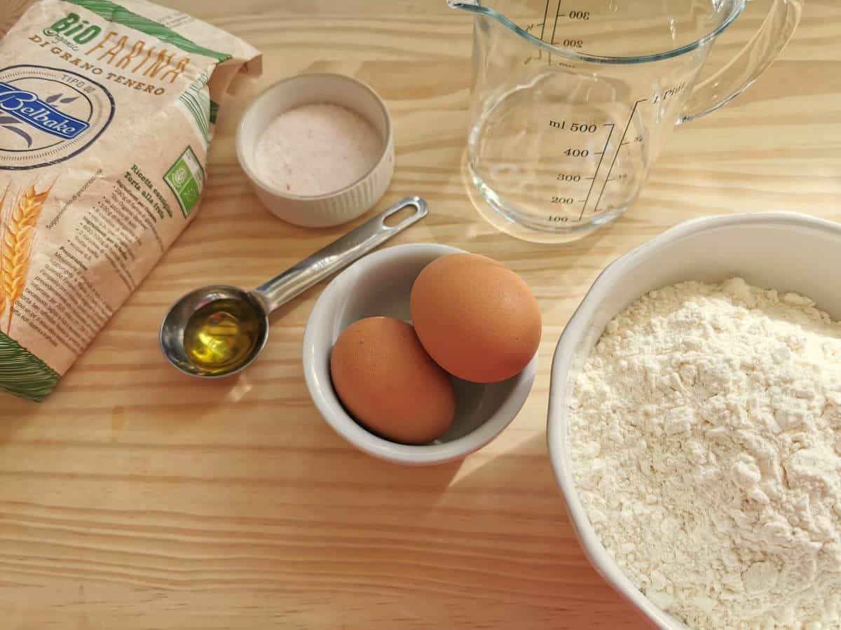 Ingredients for homemade maccheroni; flour, eggs, salt, water and tablespoon of olive oil on wood work surface.