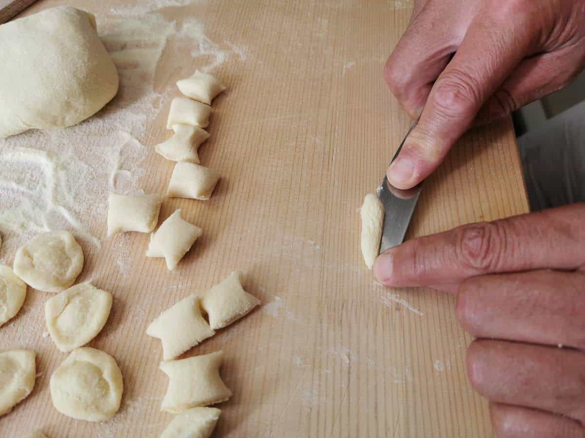 Man making homemade orecchiette on wood pastry board.