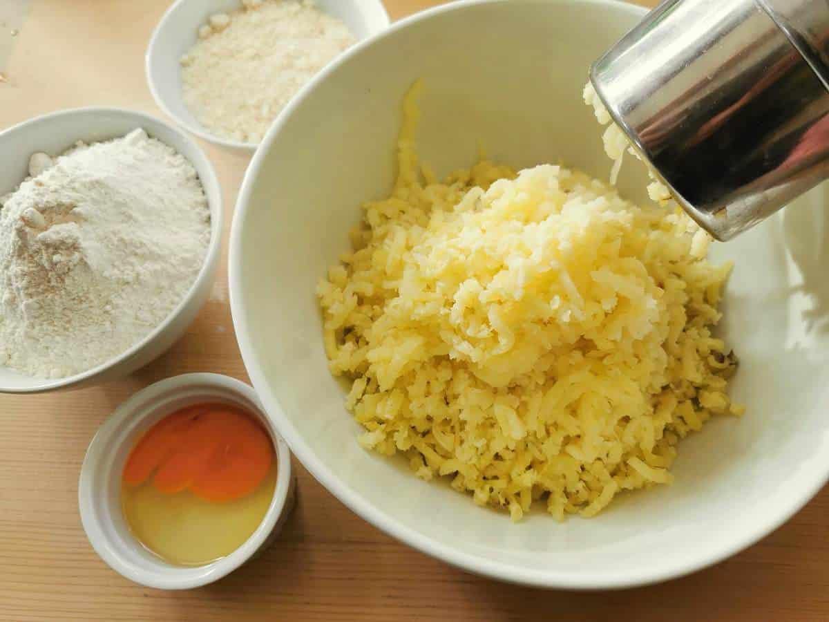 potato passed through a potato ricer into a white bowl.