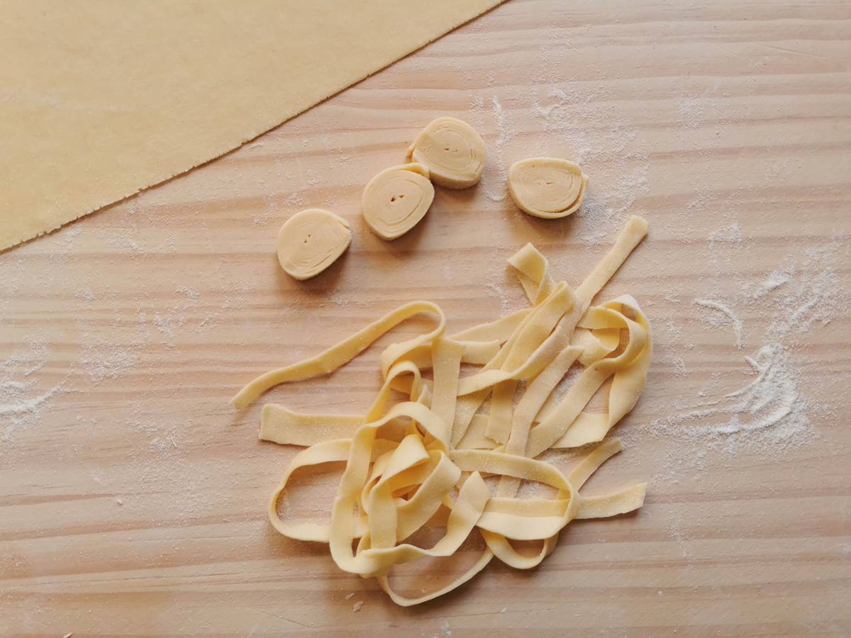 Homemade tagliatelle strands and rolled up cut rounds of pasta dough on wooden board.