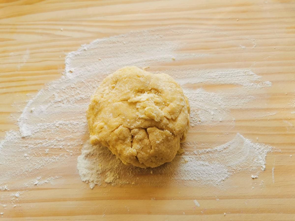 Rough ball of pasta dough on wooden board dusted with flour.