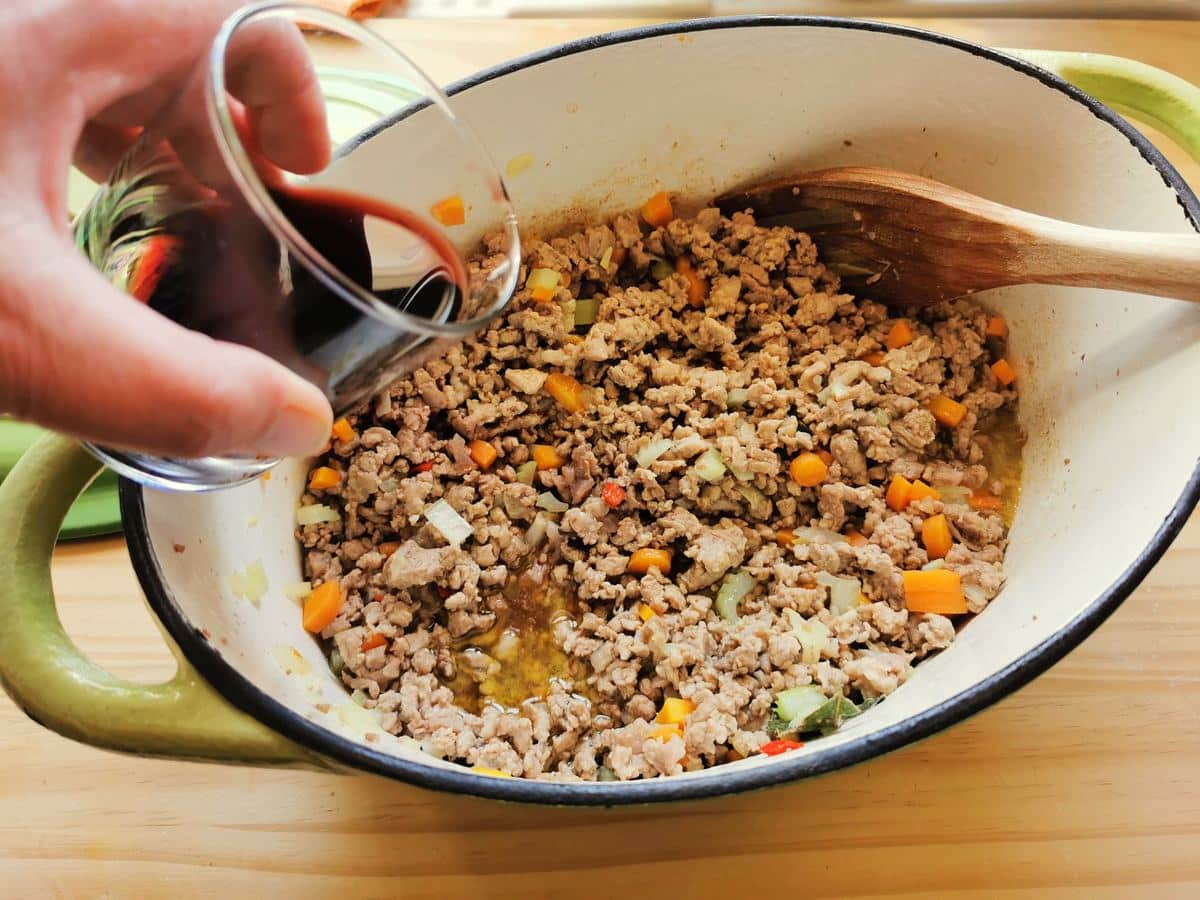 Adding red wine into the lamb and vegetables.