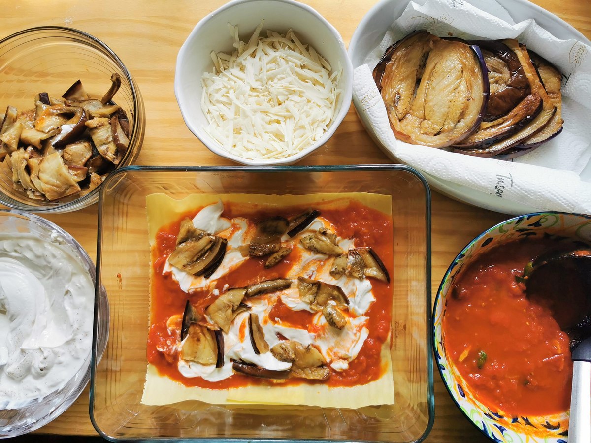 Pasta sheets, tomato sauce, ricotta cream and pieces of fried eggplant in glass oven dish to make the first layer of lasagna alla norma.