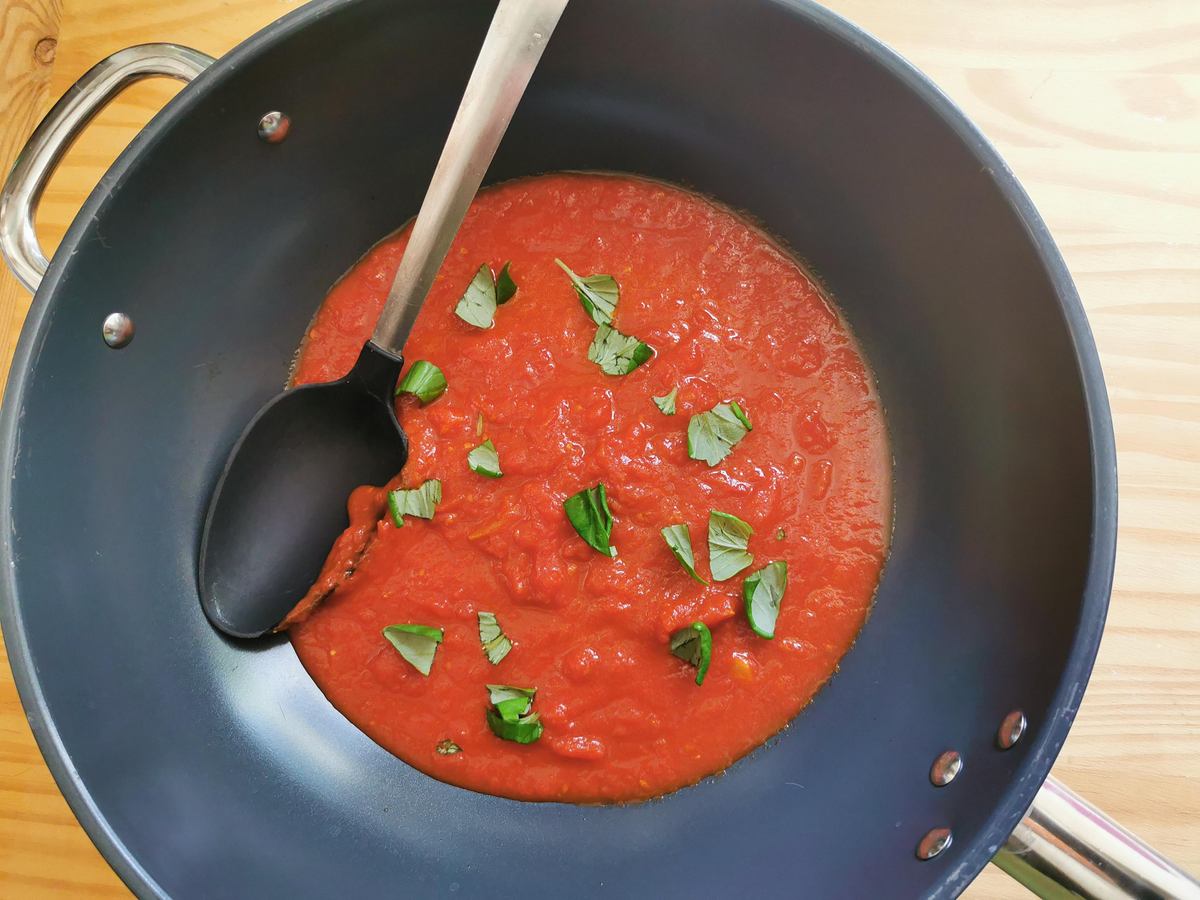 Homemade tomato sauce in deep skillet with basil leaves on top.