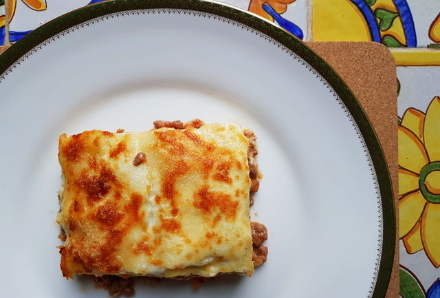 a serving of lasagne al forno with bolognese on white plate with green rim