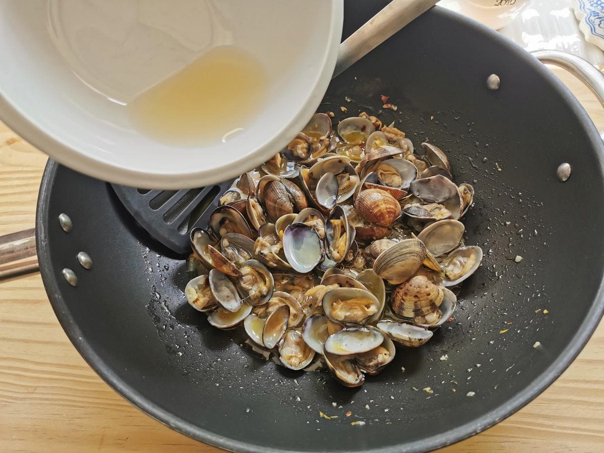 Clam cooking water being added to clams in deep frying pan.