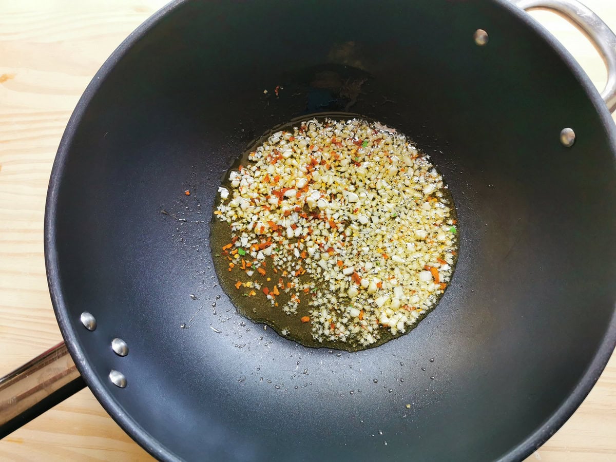 Chopped garlic and peperoncino flakes cooking in deep frying pan.