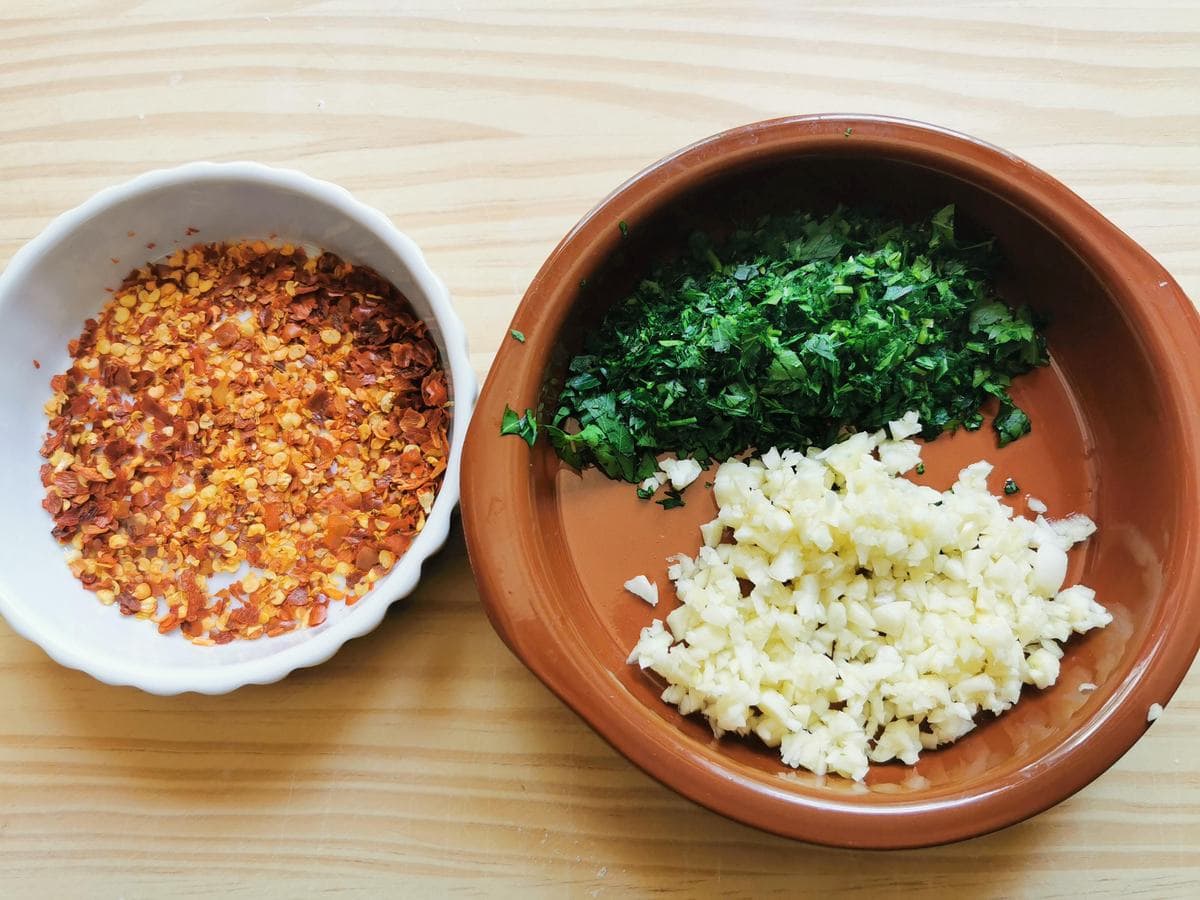 Chopped fresh parsley and garlic in small bowl. Red pepper flakes in small bowl.