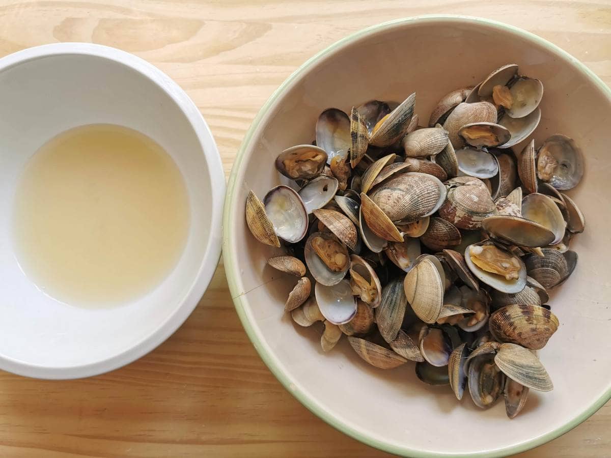 Cooked clams in large bowl and filtered clam cooking in small white bowl.