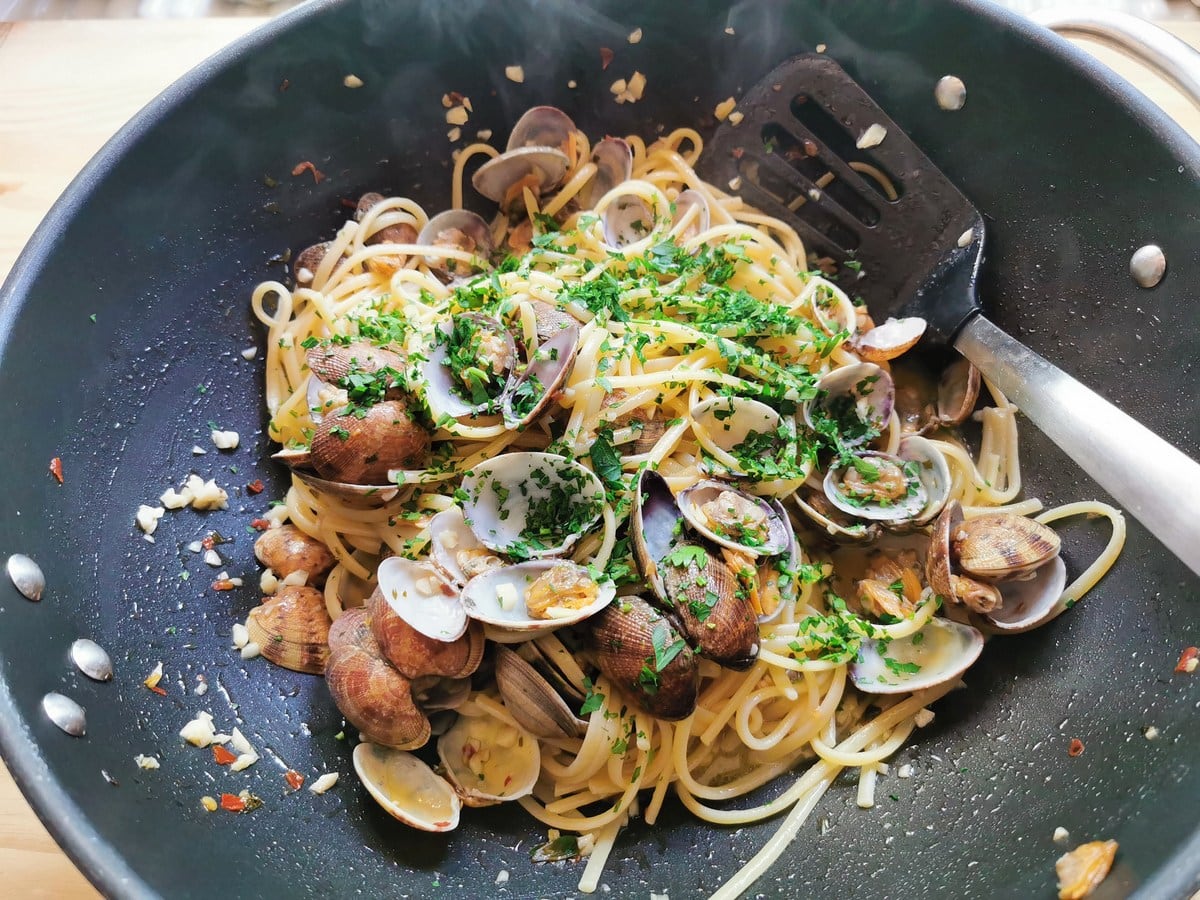 Chopped parsley in pan with linguine and clams.