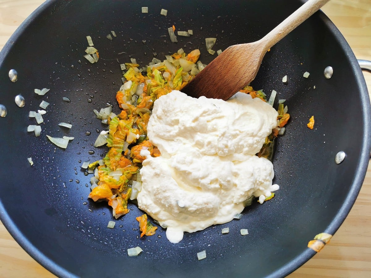 Mixing the softened zucchini flowers and onions with the ricotta sauce.