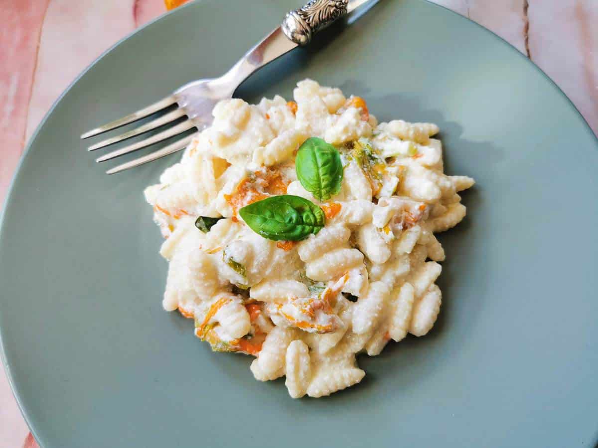 Malloreddus pasta with zucchini flowers and a ricotta sauce on a plate.