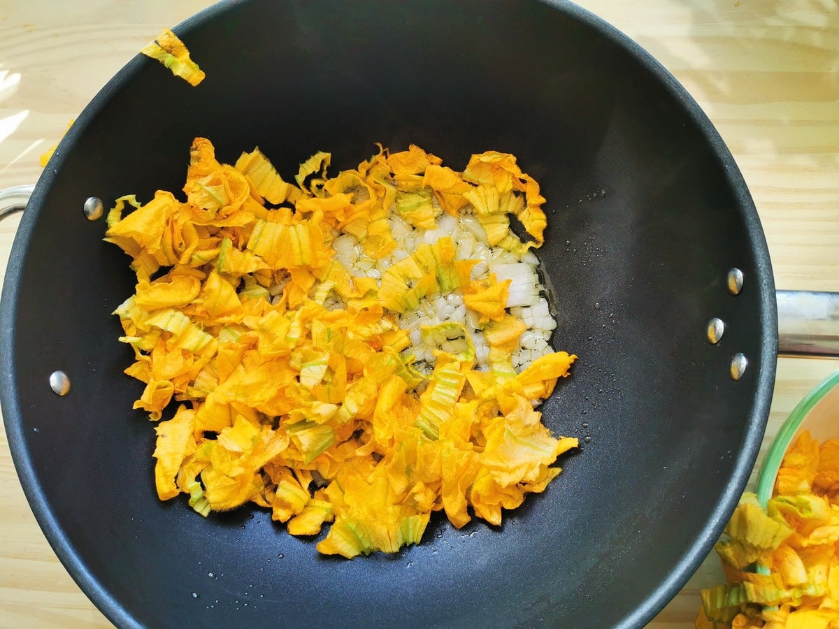 Cooking zucchini flowers and onions in a pan.