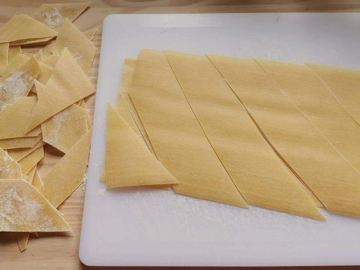 Fresh pasta sheet cut into rhomboids on white chopping board.