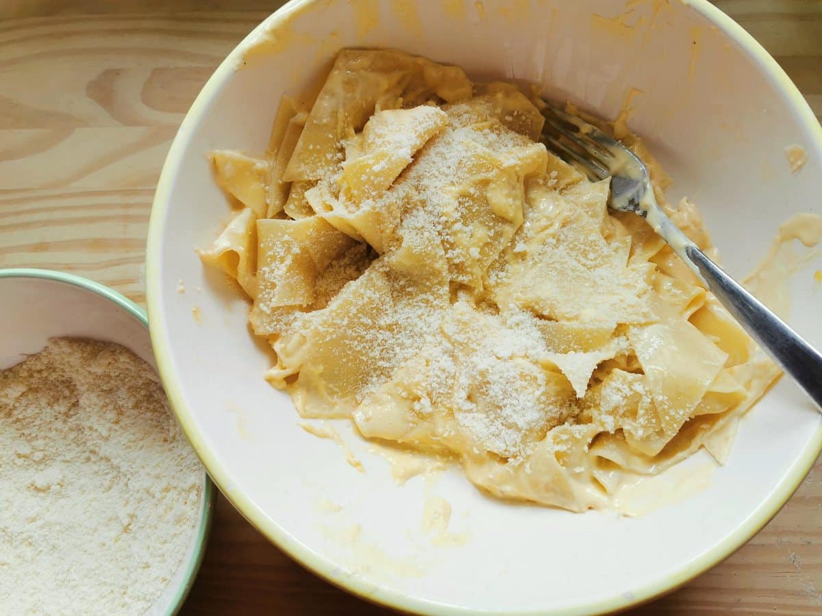 Grated grana added to maltagliati pasta with mascarpone in white bowl