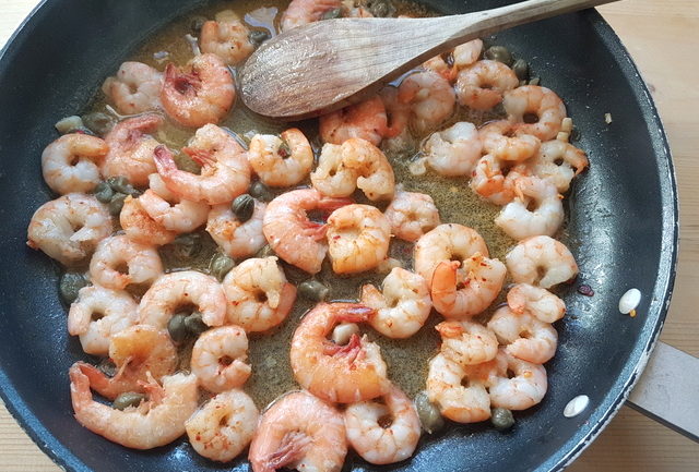 peeled prawn tails, garlic and capers cooking in frying pan