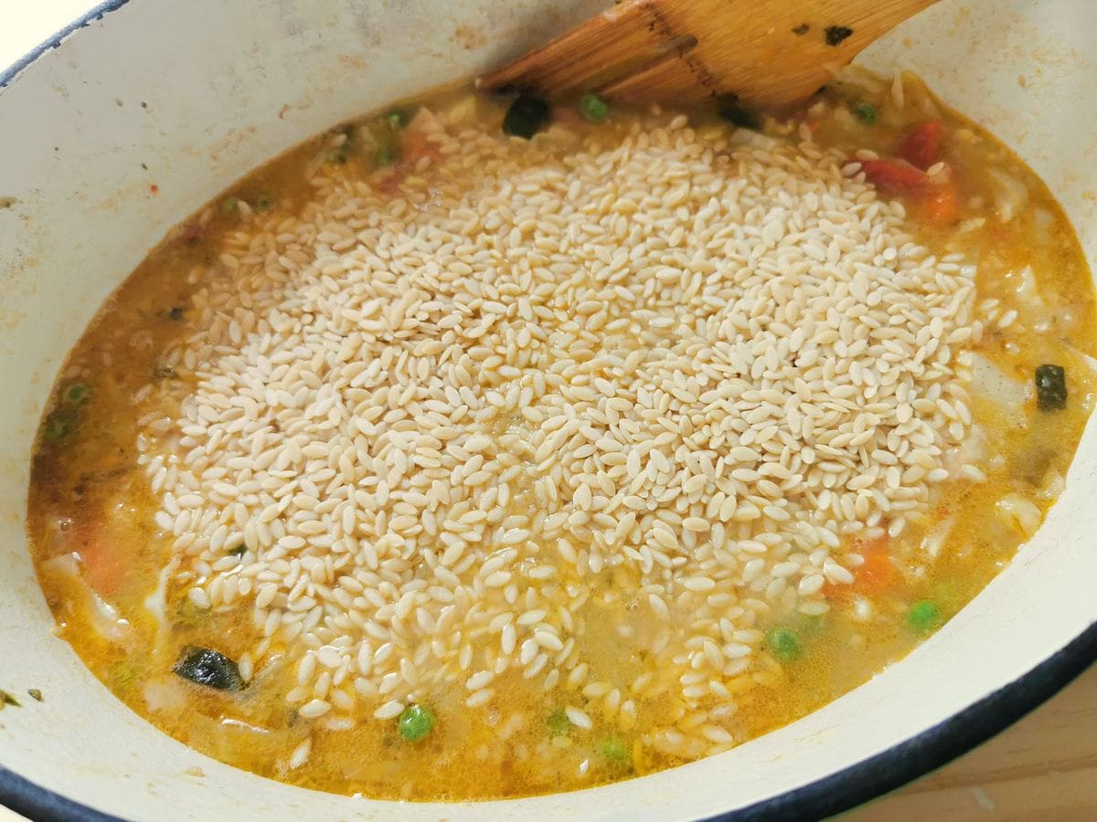 Orzo (risoni) pasta added to minestrone Milanese in Dutch oven.