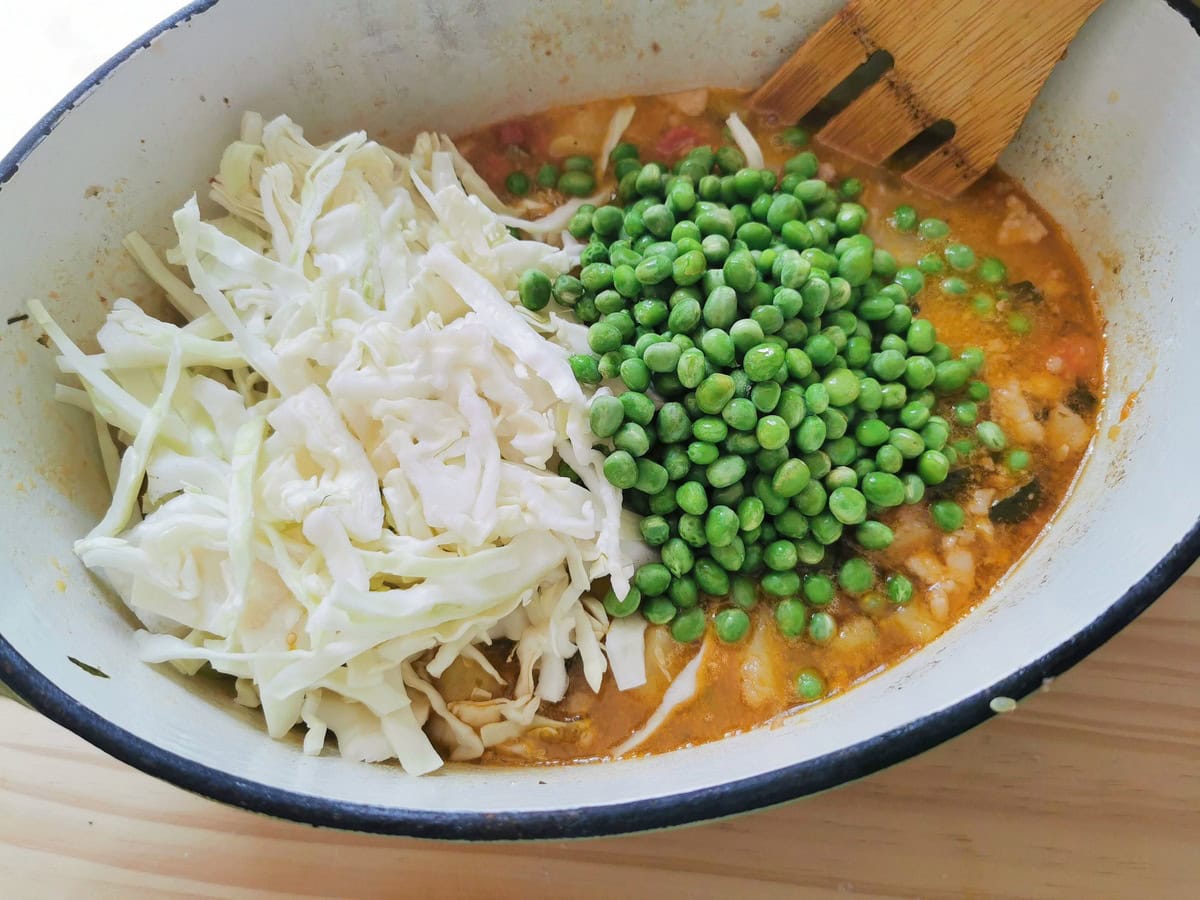 Peas and sliced cabbage added to the minestrone cooking in a Dutch oven.