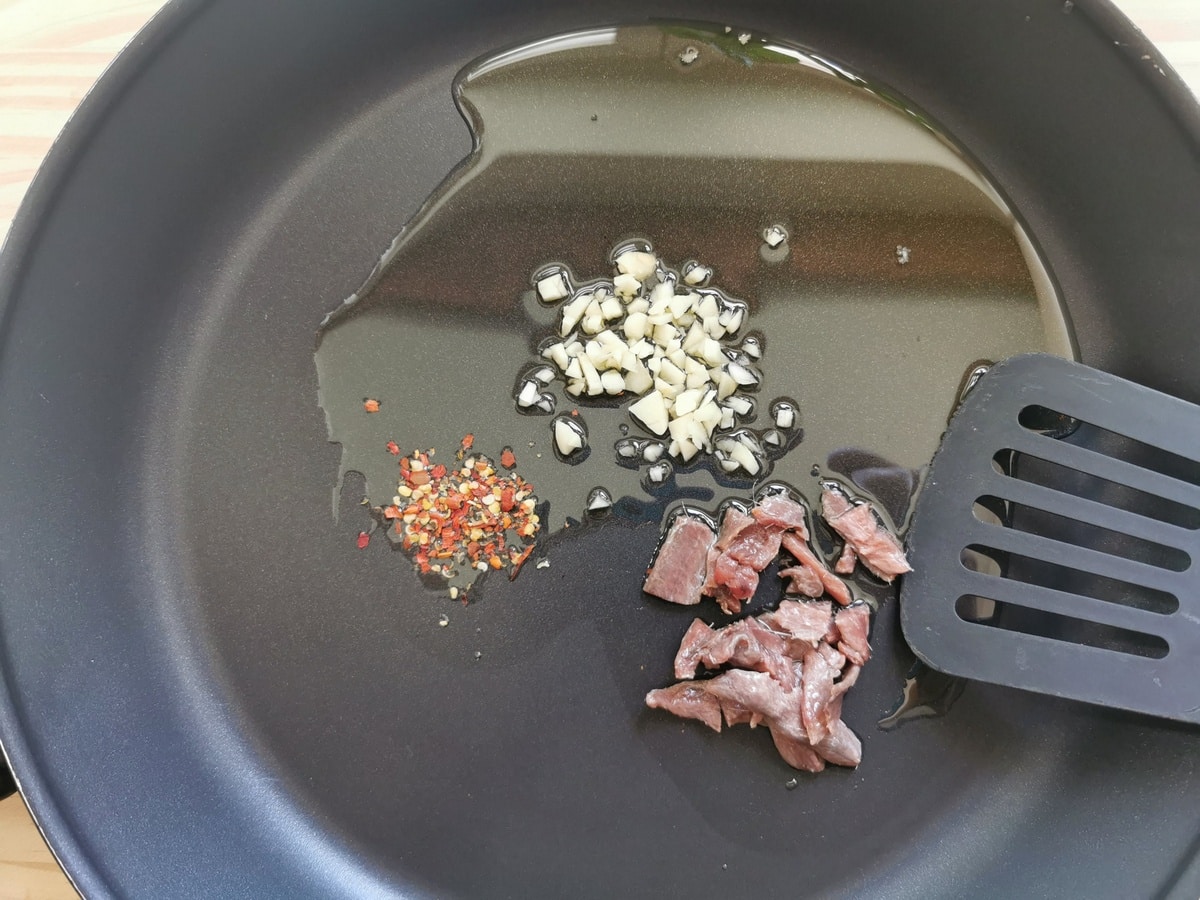 Chopped garlic, dried peperoncino flakes, and anchovy fillets in a pan with olive oil.