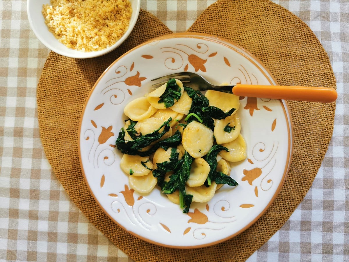 Orecchiette with broccoli rabe in a bowl next to breadcrumbs.