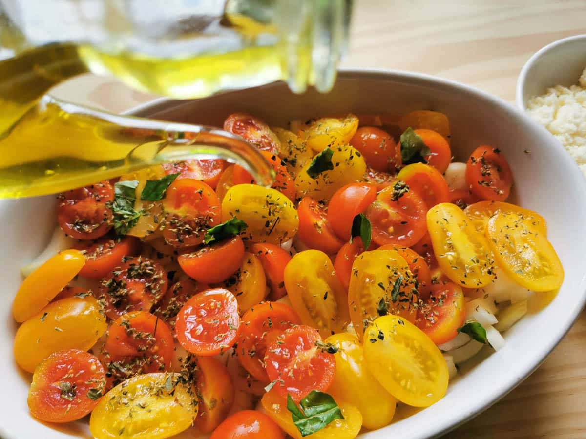 Pouring olive oil into a baking dish with cherry tomatoes