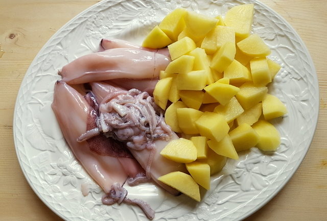 peeled and cut potatoes and cleaned calamari on a white plate