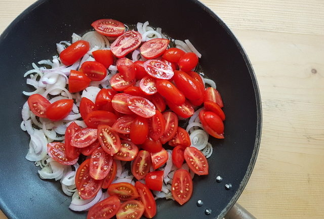 sliced red onions and halved date tomatoes in skillet