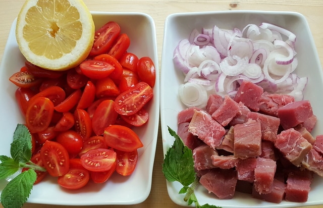 sliced red onions and cubed tuna in white bowl plus halved date tomatoes and half a lemon in another white bowl.