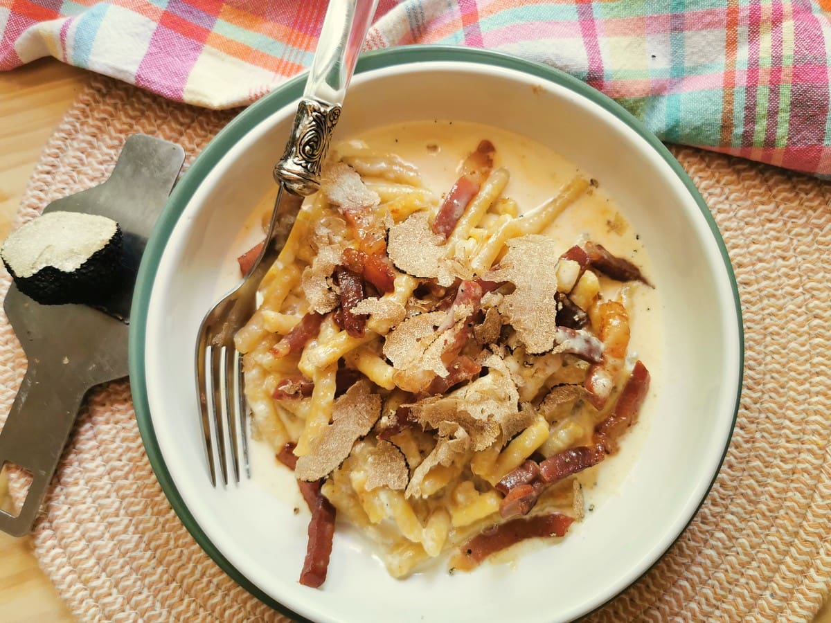 Plated passatelli with prosciutto in white bowl with truffle shaving on top.