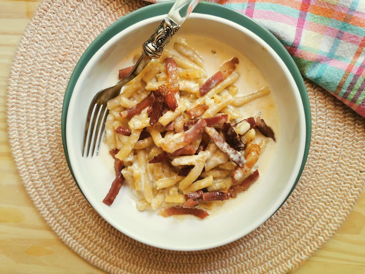 Passatelli pasta with prosciutto and Parmigiano cream in white bowl.