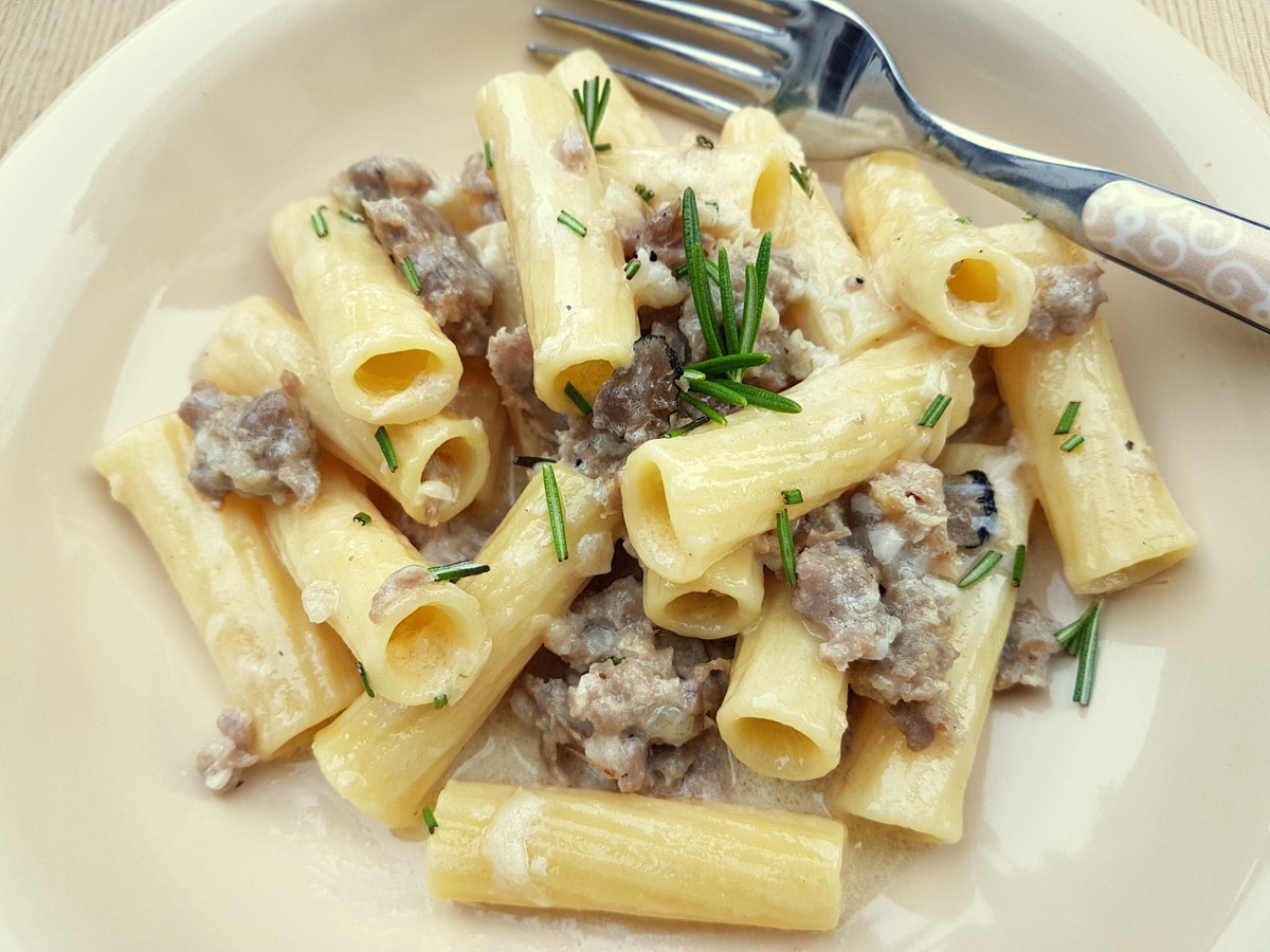 A serving of creamy pasta alla Norcina in a light beige bowl with a fork.