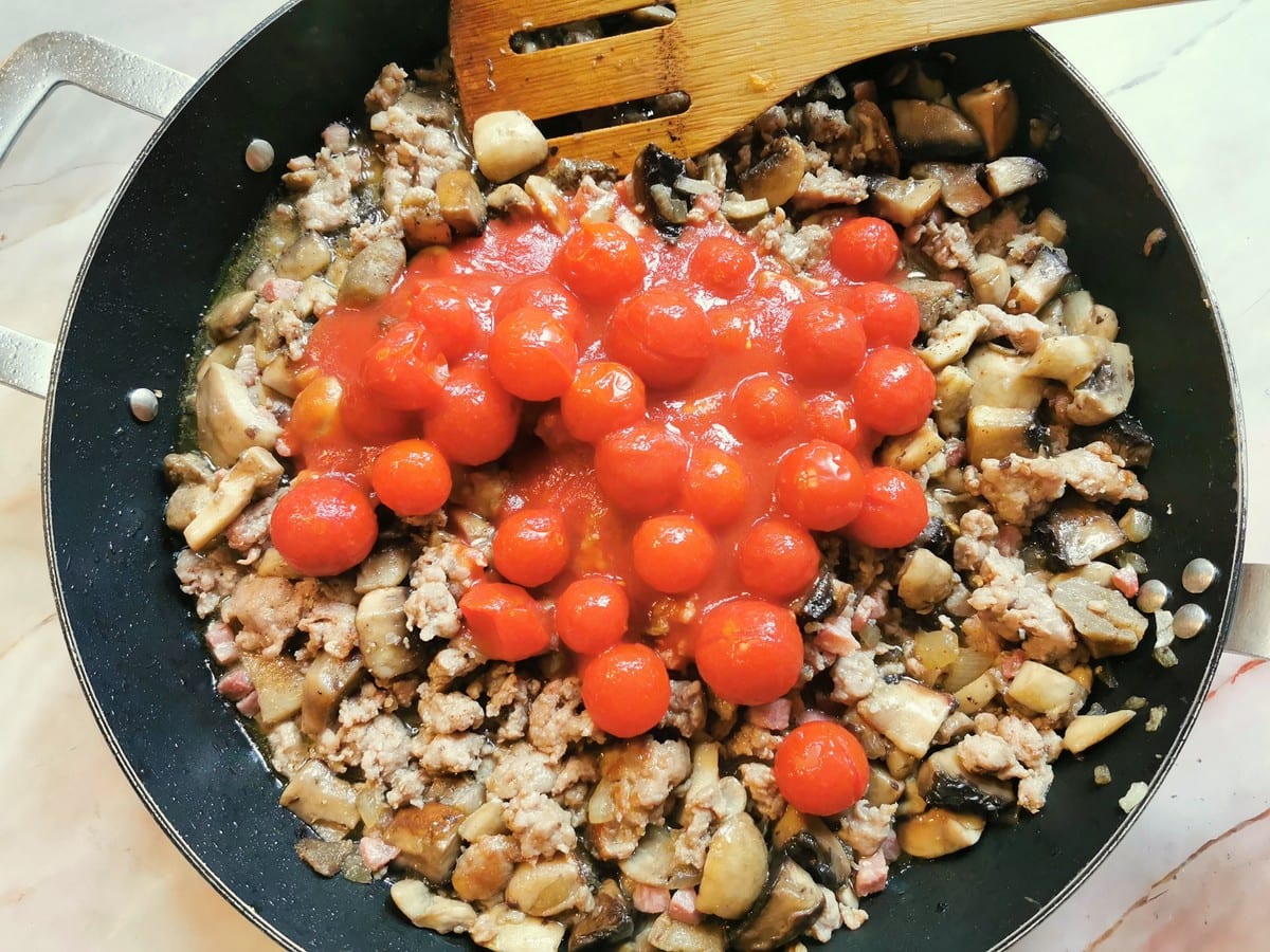Canned cherry tomatoes added to sausage, pancetta and mushrooms in skillet.
