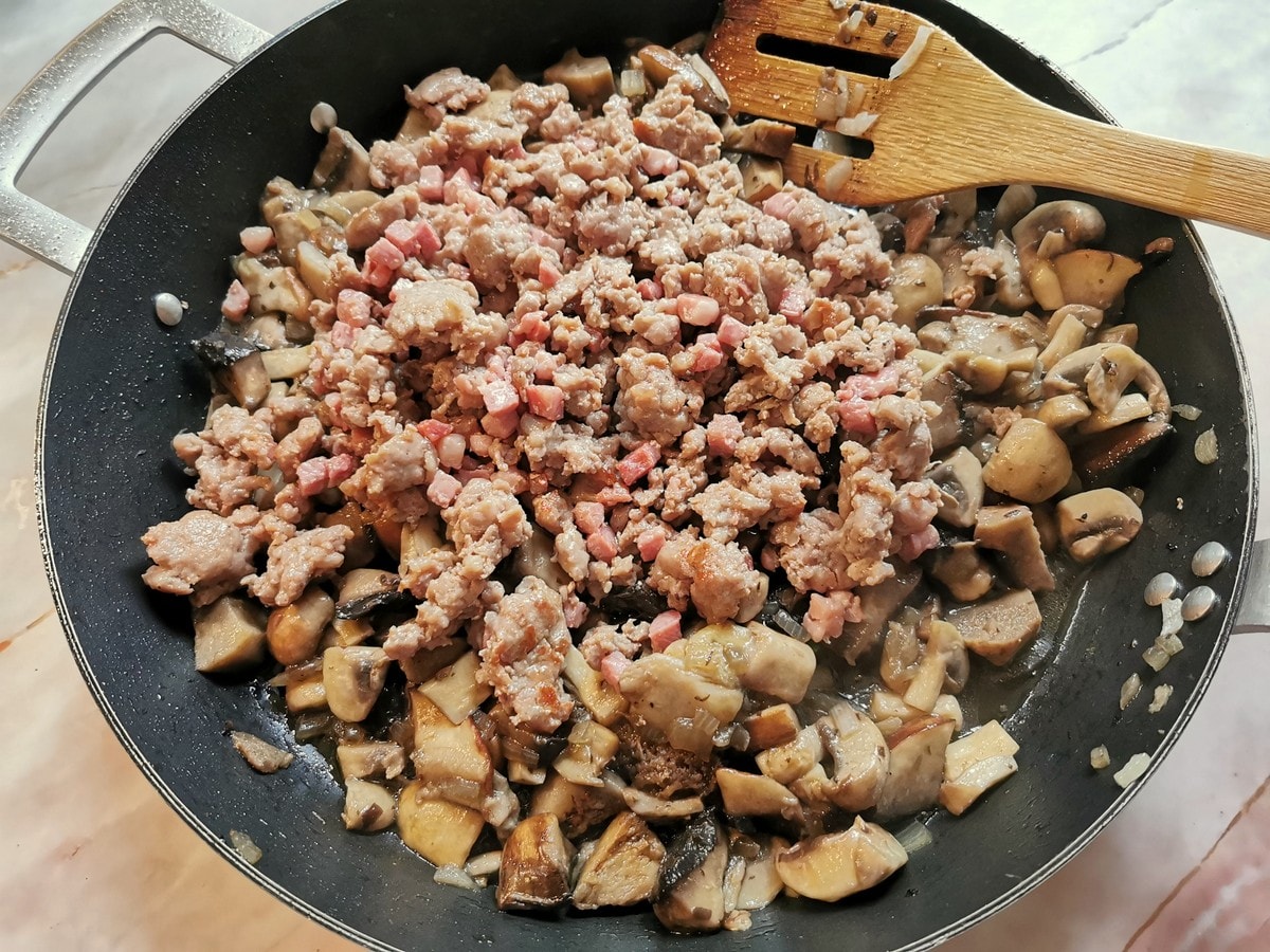 Cooked mushrooms in skillet with browned sauage meat and pancetta.