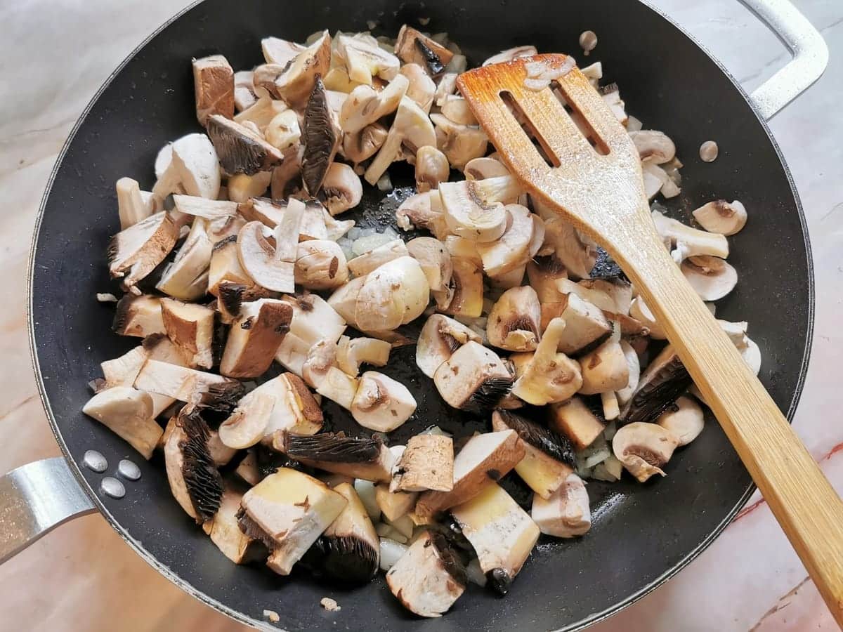 Fresh mushroom pieces in skillet with cooked onions.