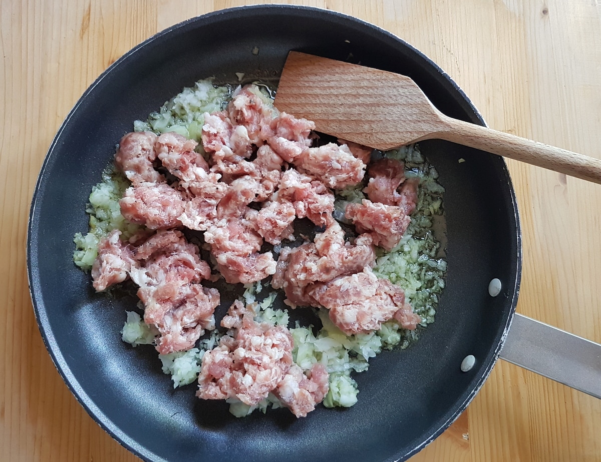 Crumbled sausage and chopped onion in a pan.