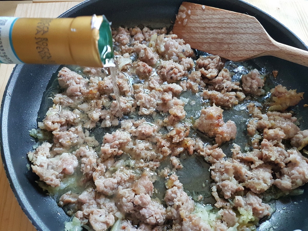 Crumbled sausage, chopped onion and white wine in a pan.