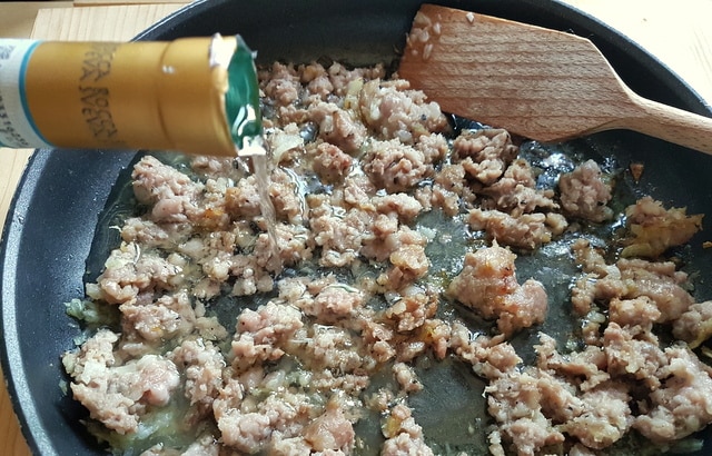 pouring wine into browned sausage meat in frying pan