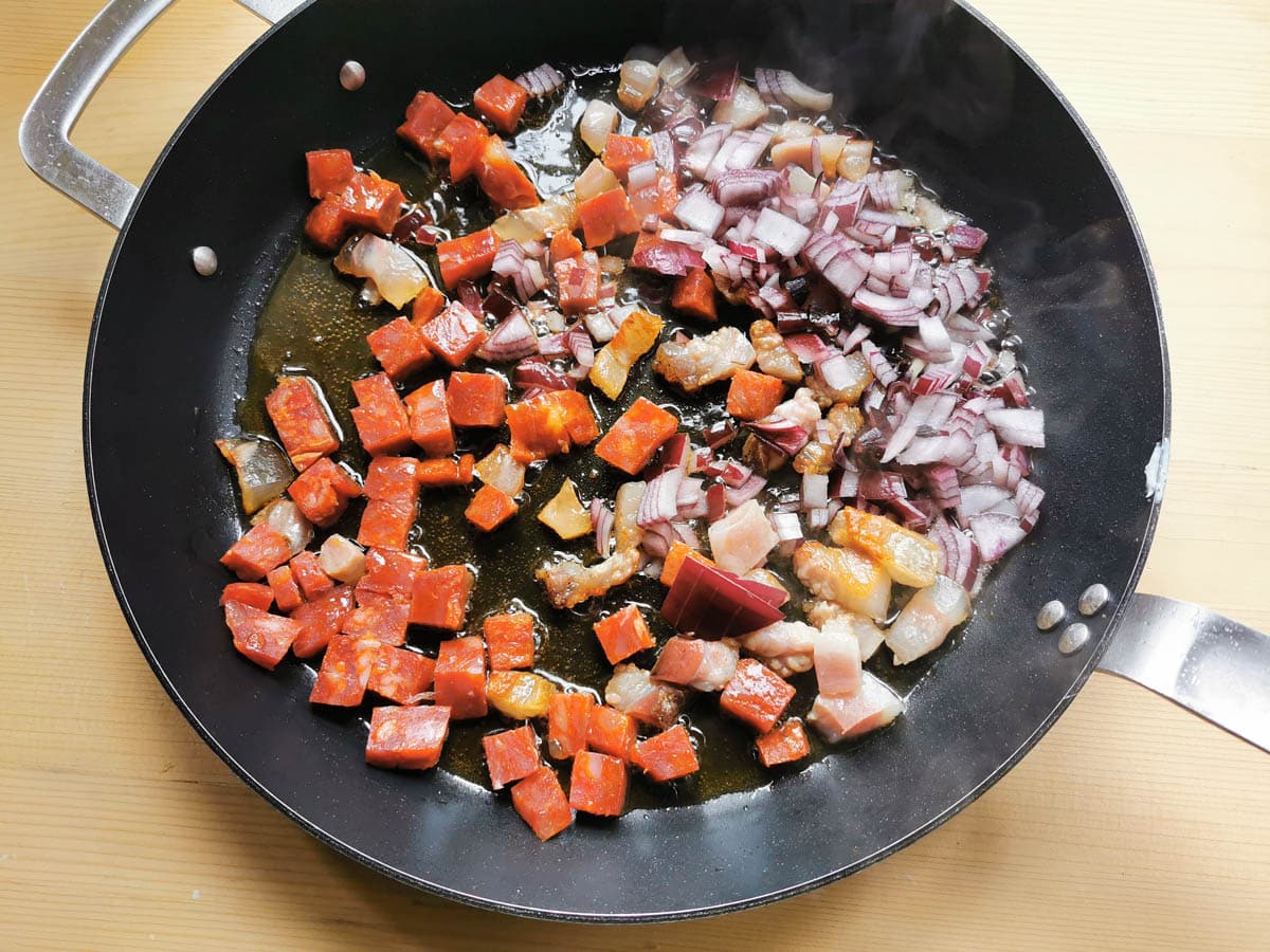 Guanciale, soppressata, and peperoncino flakes cooking in a pan.